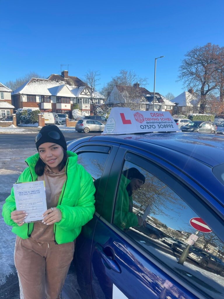 A joyful learner driver confidently taking the wheel of a car during a Derin Driving School lesson, with Barnet's scenic streets in the background